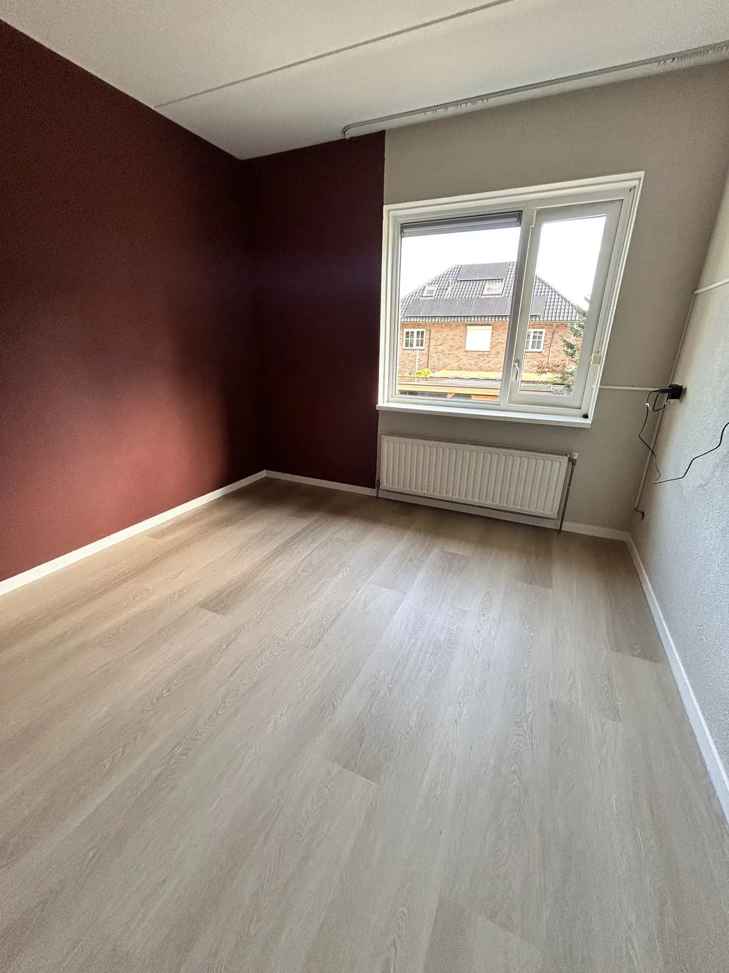 Slaapkamer met een lichte pvc-vloer en een donkerrode wand